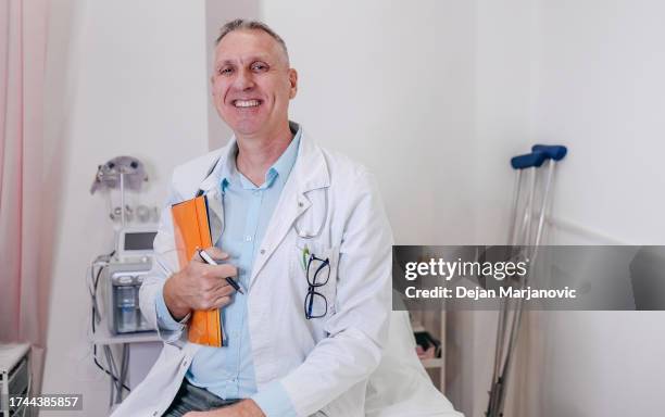 porträt eines arztes mittleren alters, der im krankenhaus auf dem bett sitzt - ordination stock-fotos und bilder