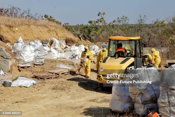 Bucket loader and workers in protective suits and gas masks are pictured during the cleaning of the hazardous waste storage facility which contains...