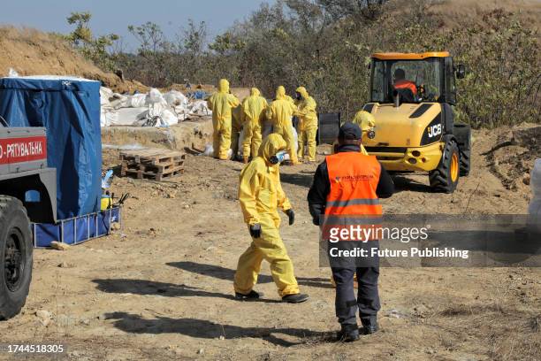 Bucket loader and workers in protective suits and gas masks are pictured during the cleaning of the hazardous waste storage facility which contains...