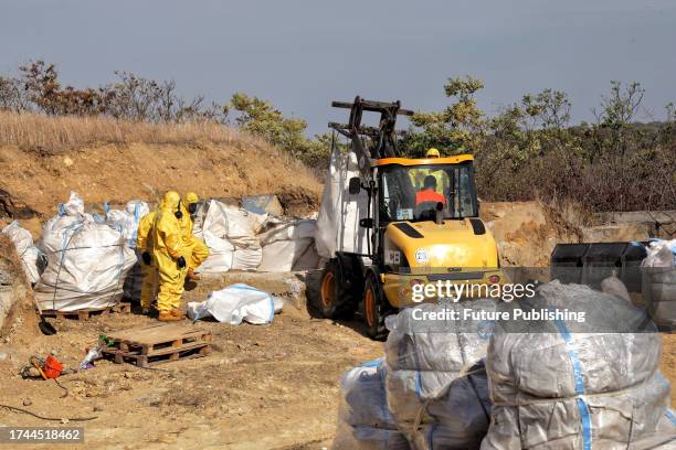 Bucket loader and workers in protective suits and gas masks are pictured during the cleaning of the hazardous waste storage facility which contains...