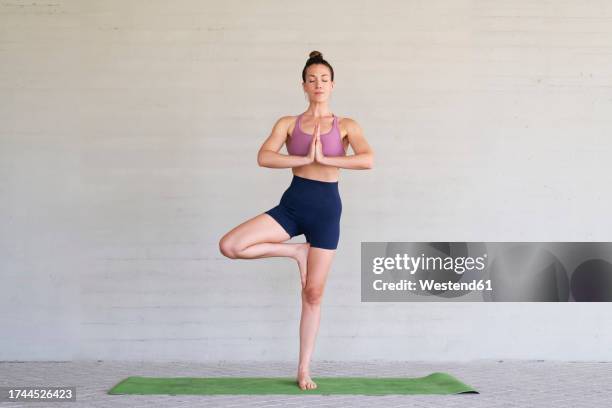 woman doing yoga standing in front of wall - tree position stock pictures, royalty-free photos & images