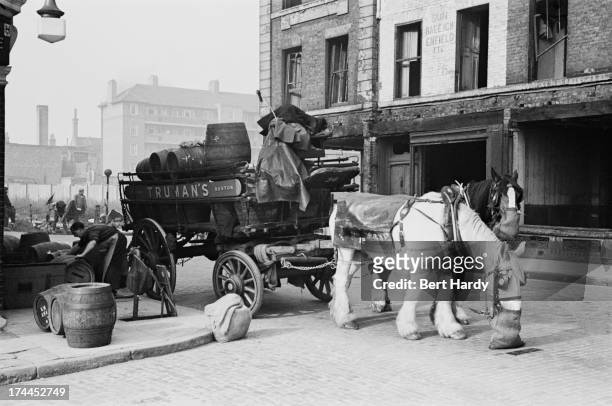 Men unloading barrels of beer outside a pub in the Pool of London, while their carthorse feeds from a nosebag, December 1949. Original publication:...