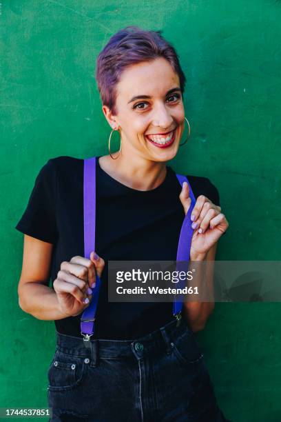 happy hipster woman holding suspenders in front of wall - suspenders stock pictures, royalty-free photos & images