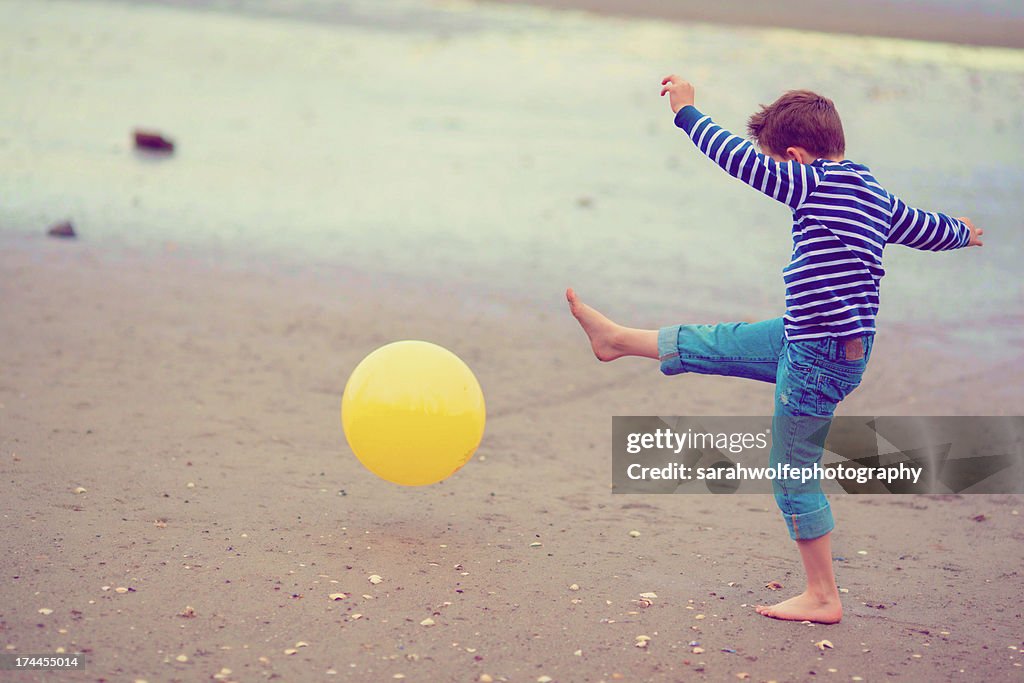 Boy kicking ball on beach