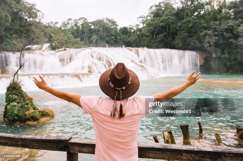 Man with arms outstretched in front of Agua Azul Cascades with trees