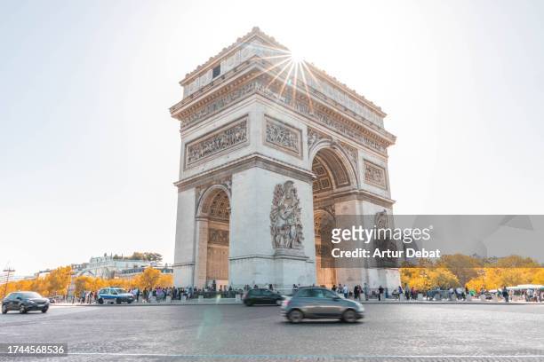 the arch de triomphe in paris with traffic in motion and sunbeam. - paris police stock pictures, royalty-free photos & images