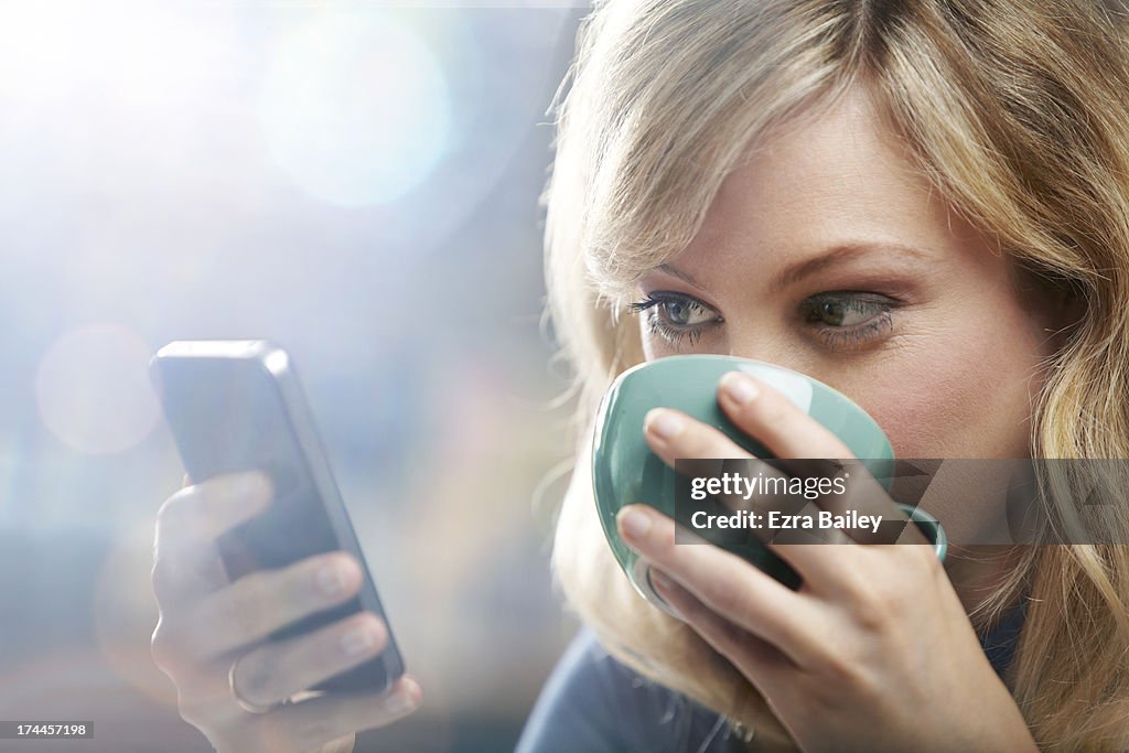 Woman using phone and drinking coffee.