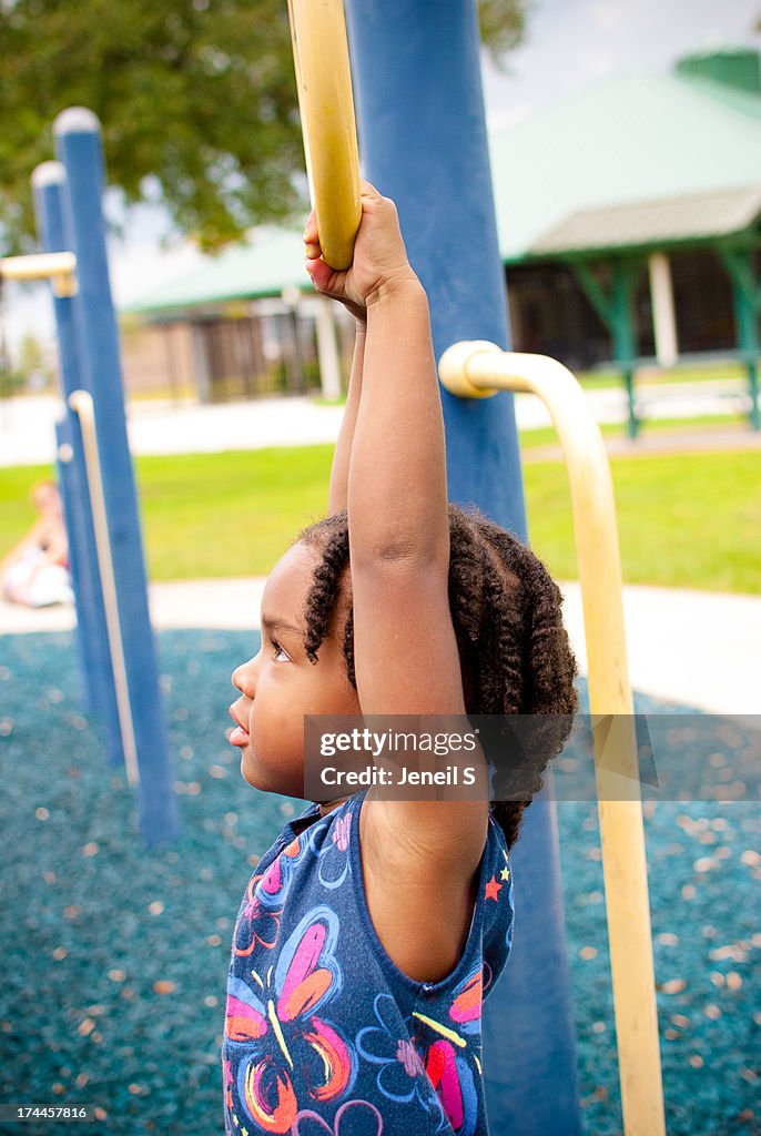 Toddler girl hanging onto bars at the park