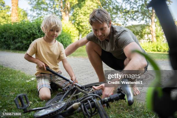 boy with father repairing bicycle at footpath - luftpumpe stock-fotos und bilder