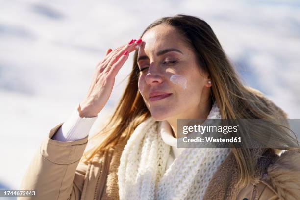 smiling woman with eyes closed applying sunscreen in winter - suntan lotion stock pictures, royalty-free photos & images