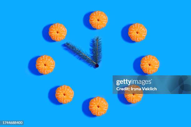 happy new year  celebration concept with clock  made of orange tangerines and green branches of the christmas tree on blue colour background. - orange alarm clock stock pictures, royalty-free photos & images