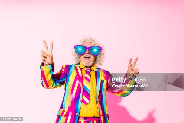 happy senior man wearing oversized sunglasses and gesturing peace sign - multi coloured suit stock pictures, royalty-free photos & images