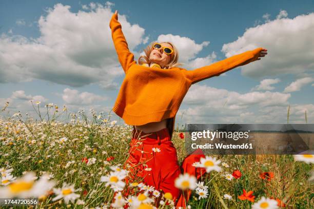 carefree woman jumping with arms raised in chamomile field - jump for joy stock pictures, royalty-free photos & images