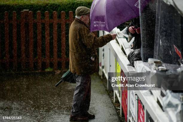 Heavy rain falls as a racegoer places a bet with the bookmakers at Wincanton Racecourse on October 19, 2023 in Wincanton, England.