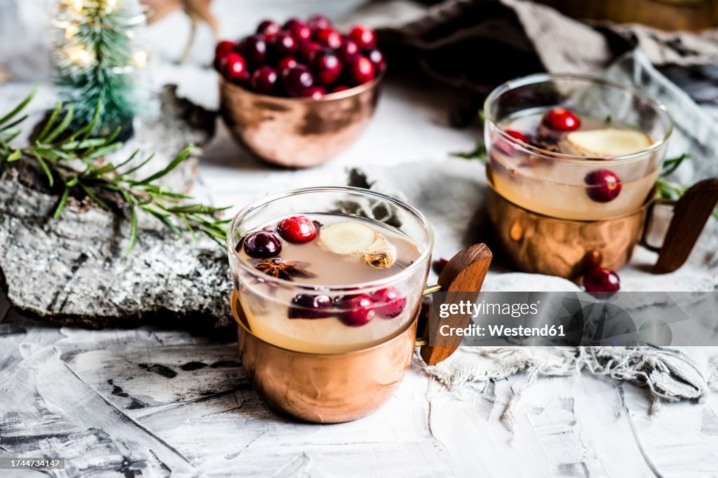 Cups of Moscow mule drink with cranberries and spices on table