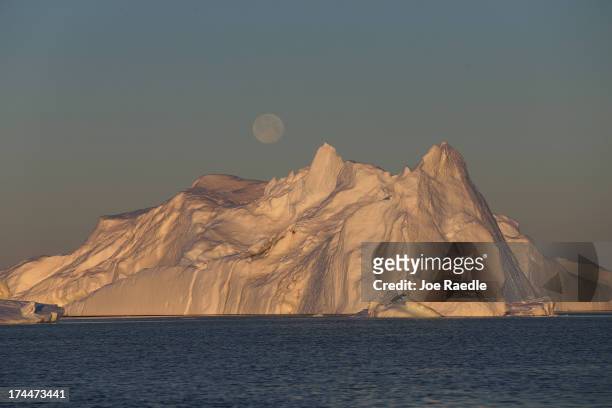 Full moon is seen over an iceberg that broke off from the Jakobshavn Glacier on July 23, 2013 in Ilulissat, Greenland. As the sea levels around the...