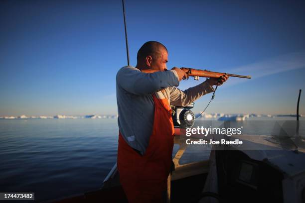 Fisherman, Inunnguaq Petersen, hunts for seal as he waits for fish to catch on the line he put out near icebergs that broke off from the Jakobshavn...