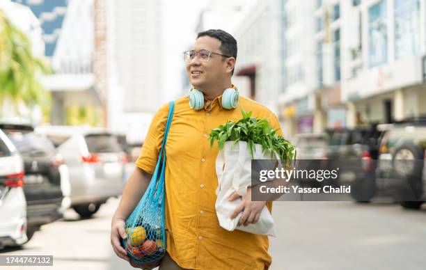 asian man walking on street with groceries on hands - överviktig bildbanksfoton och bilder