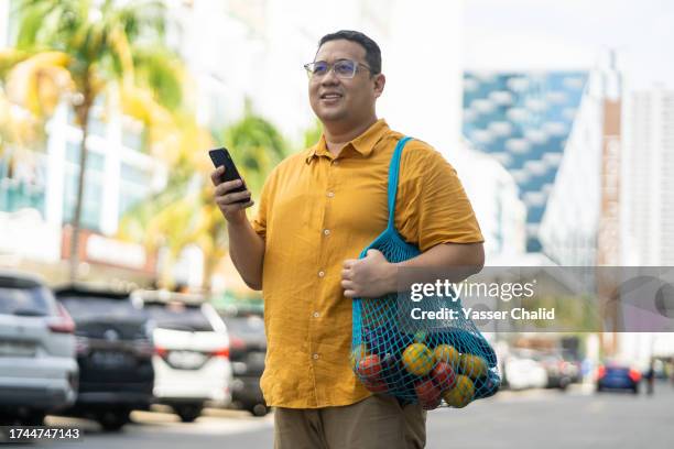 asian man standing with mesh bag on hand - chubby man shopping stock pictures, royalty-free photos & images