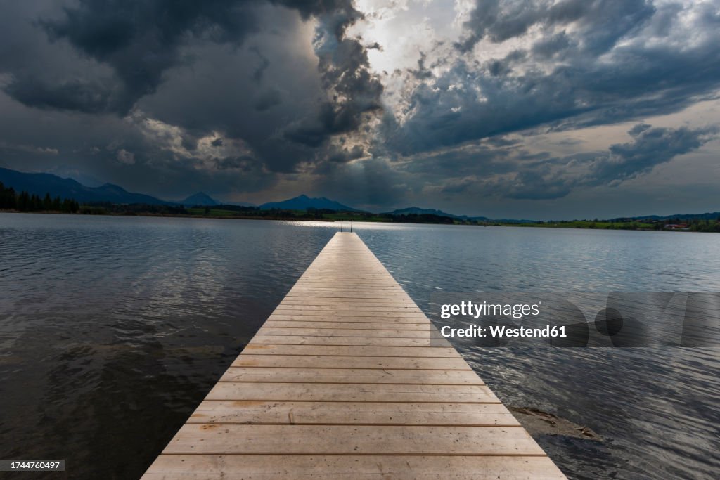 Germany, Bavaria, Hopfen am See, Storm clouds over empty jetty on Hopfensee lake
