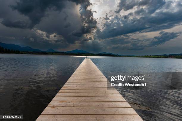 germany, bavaria, hopfen am see, storm clouds over empty jetty on hopfensee lake - lakeshore stock pictures, royalty-free photos & images