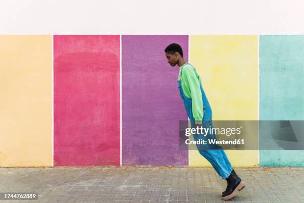 young woman leaning on tiptoes in front of multi colored wall - tiptoe stock-fotos und bilder