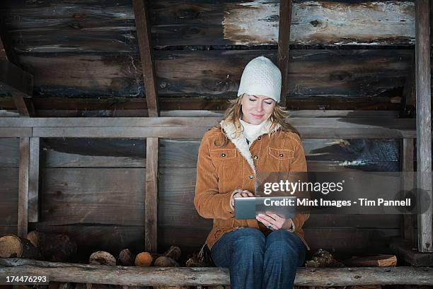 an organic farm in upstate new york, in winter. a woman sitting in an outbuilding using a digital tablet.  - winter coat stock pictures, royalty-free photos & images