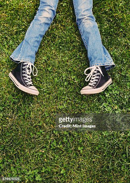 a ten year old girl lying on the grass. cropped view of her lower legs. wearing sneakers and faded blue jeans. - tween heels stock pictures, royalty-free photos & images