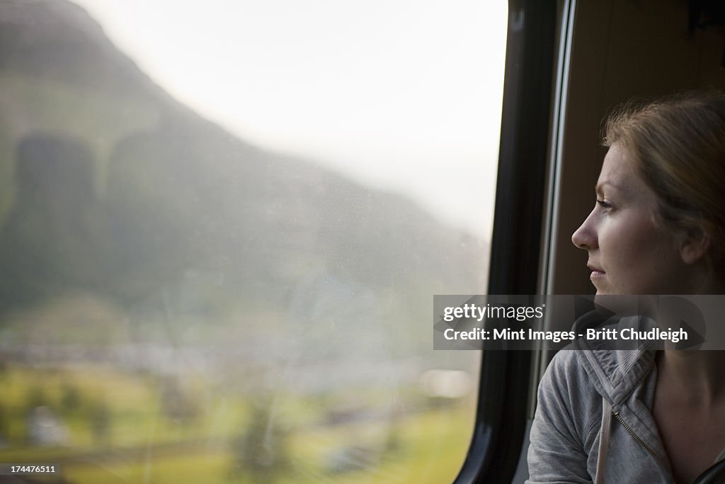 A woman sitting by a train window looking out at the landscape.