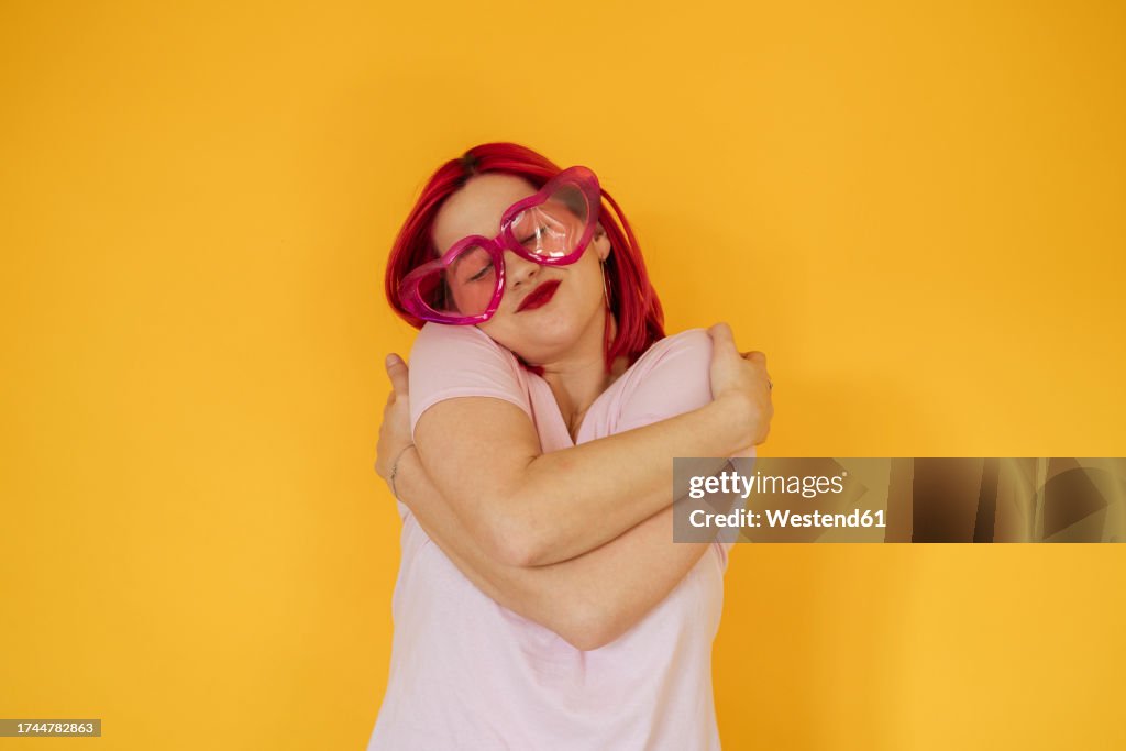 Smiling woman wearing heart shaped sunglasses hugging self