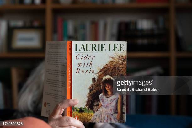 Woman sits in her living room and reads a copy of Laurie Lee's seminal memoir, 'Cider With Rosie', on 20th October 2023, in London, England.