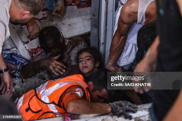 Graphic content / Rescuers pull out an injured young girl and a man from under the rubble of a supermarket hit by an Israeli strike on the Rafah...