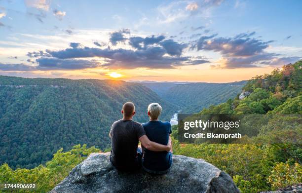 couple enjoying a vibrant sunset view from beauty mountain in new river gorge national park during the fall season in the appalachian mountains of west virginia, usa. - west virginia scenic stock pictures, royalty-free photos & images