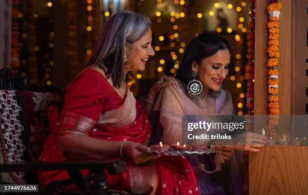 madre mirando a su hija colocando diyas en casa durante diwali - diya oil lamp fotografías e imágenes de stock