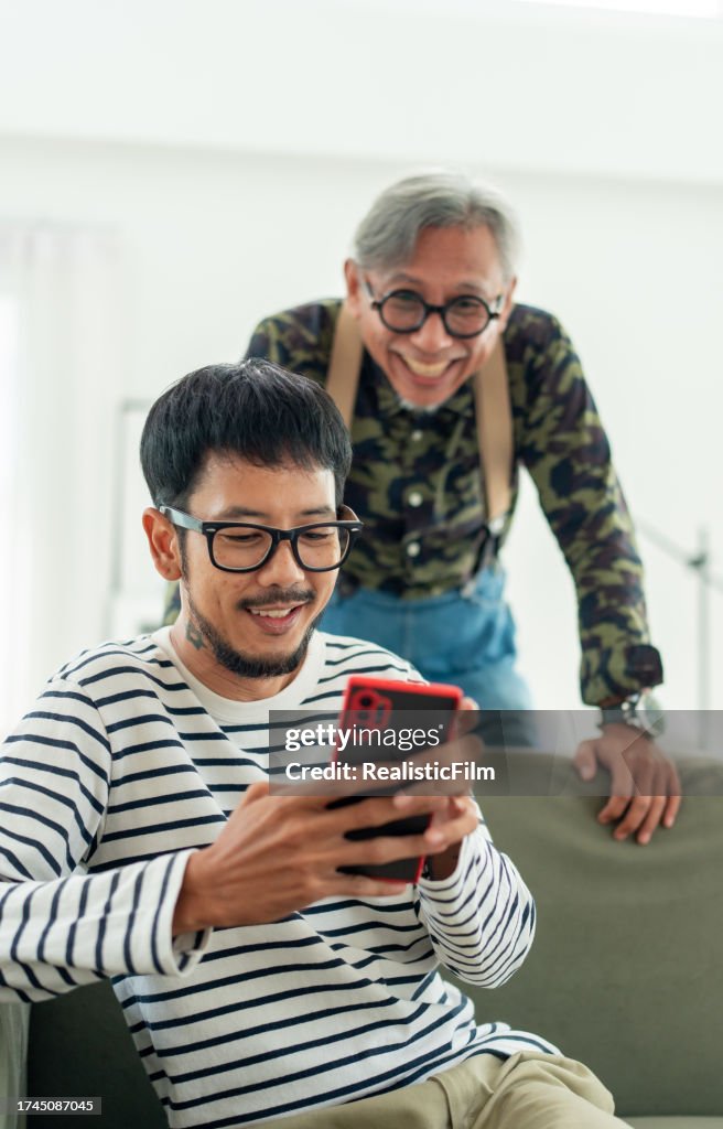 Generationenübergreifende Bindung: Ungezwungene Glücksmomente, wenn sich ein asiatischer Mann und ein älterer Vater durch Technologie in ihrem Wohnzimmer verbinden.