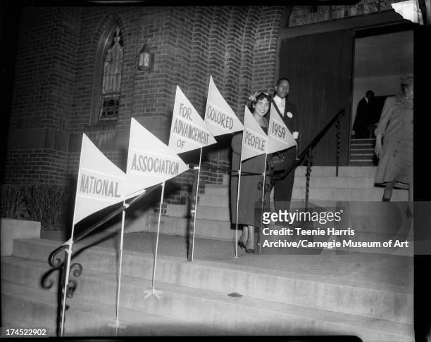 Woman and Matthew Moore Sr. Standing behind flags inscribed 'National, Association, For Advancement of, Colored, People ' on steps of Wesley Center...