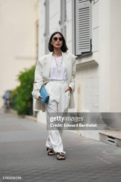 Heart Evangelista wears sunglasses, multiple necklaces, a white t-shirt, a white oversized blazer jacket, white wide leg suit pants, a blue Hermes...