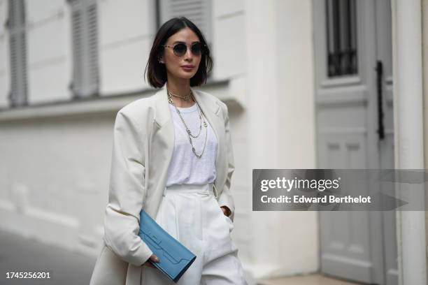 Heart Evangelista wears sunglasses, multiple necklaces, a white t-shirt, a white oversized blazer jacket, white wide leg suit pants, a blue Hermes...