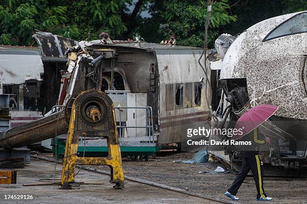 Man with an umbrella walks next to parts of a train stored in a warehouse in Escravitude, 20 km from Santiago de Compostela after a train crash...