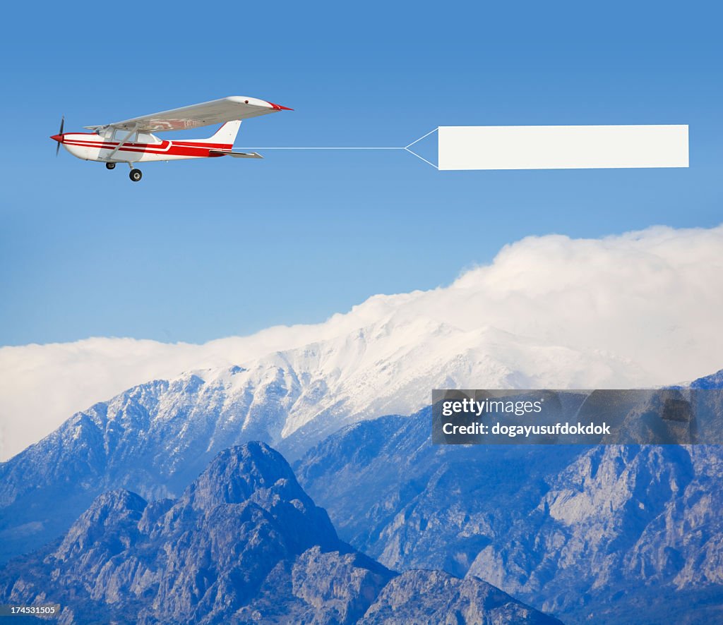 A small airplane towing a banner over a mountain landscape