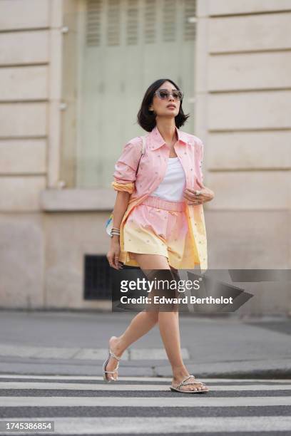 Heart Evangelista wears sunglasses, a white t-shirt from Paco Rabanne, a pastel / pale pink and yellow oversized shirt, matching mini shorts, silver...