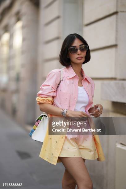 Heart Evangelista wears sunglasses, a white t-shirt from Paco Rabanne, a pastel / pale pink and yellow oversized shirt, matching mini shorts, a white...