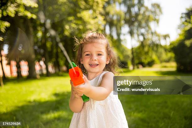 little girl enjoying summertime with squirt gun - squirt stockfoto's en -beelden