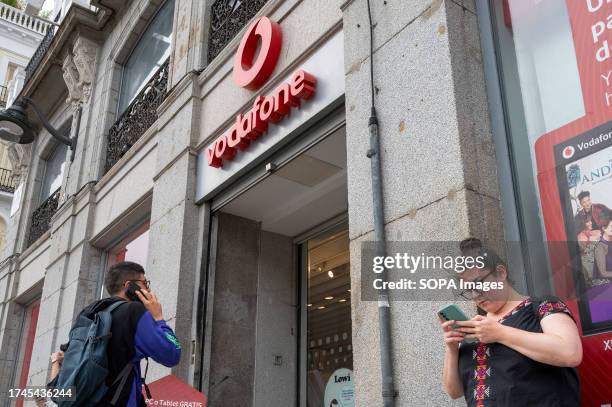 People are seen using their smartphones outside the British multinational telecommunications corporation and phone operator, Vodafone, store in Spain.