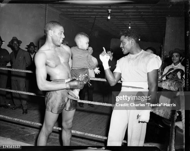 Boxer Ezzard Charles pointing at baby held by another boxer, in boxing ring in Uptown Gym, Pittsburgh, Pennsylvania, February 1950.