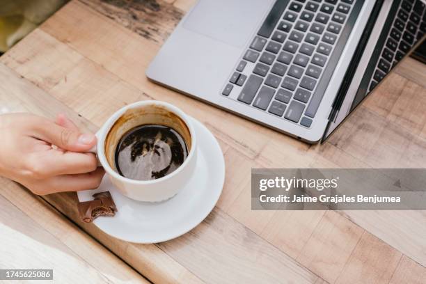 closeup of hand holding cup of coffee next to laptop - table font view stock pictures, royalty-free photos & images