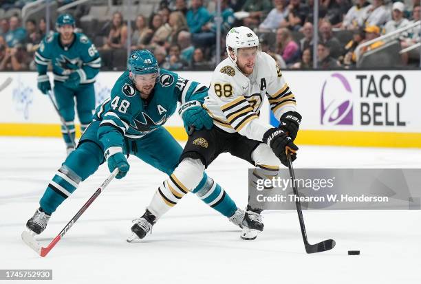 David Pastrnak of the Boston Bruins skates up ice with the puck pursued by Tomas Hertl of the San Jose Sharks during the first period at SAP Center...