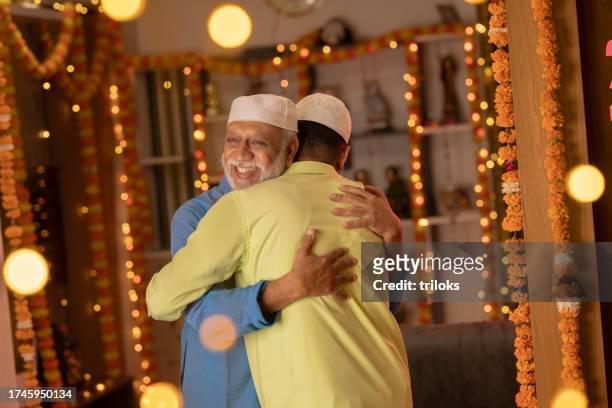 vater und sohn mit totenkopfmützen umarmen sich während eid-ul-fitr - ramadan in india stock-fotos und bilder