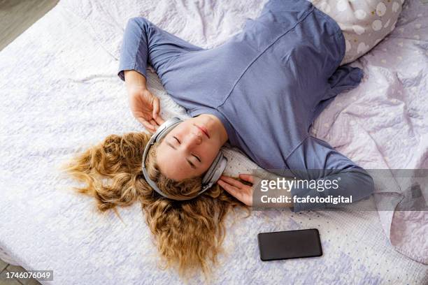 ruhiges teenager-mädchen mit geschlossenen augen verbringt zeit damit, musik zu hören, die auf ihrem bett liegt - child in bed clothed stock-fotos und bilder
