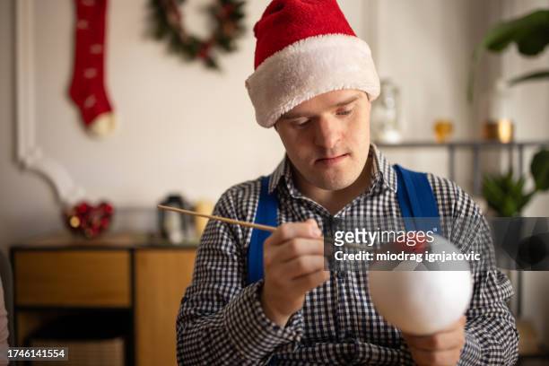 portrait of a man with down syndrome decorating a christmas ornament at home - christmas tree brush stock pictures, royalty-free photos & images